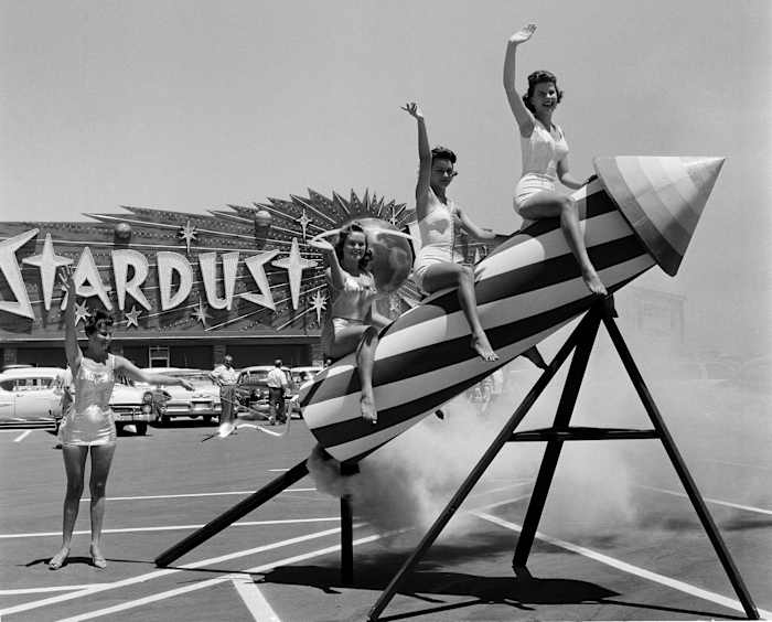 A black-and-white photo of three women sitting on a rocket outside of the Stardust casino in Las Vegas.